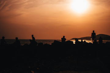 silhouettes of people resting on beach by the sea against sunset