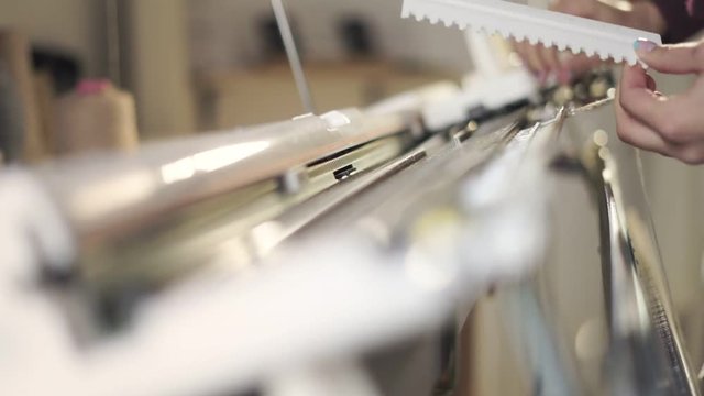 Female hands preparing weaving machine for work at factory. Close up woman regulating loom machine for knitting fabric in workshop. Knitting machine production cloth
