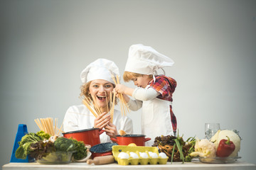 Mom and kid with smiling face cooking spaghetti together.