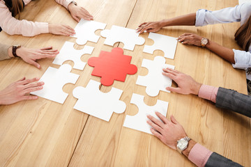 partial view of multiracial business people collecting blank puzzles at wooden table, teamwork...