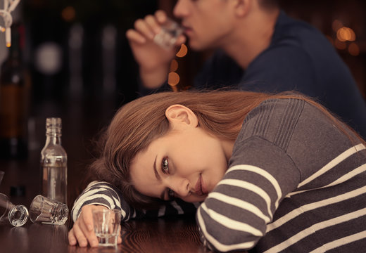 Young woman with empty glass lying on bar counter. Alcoholism problem