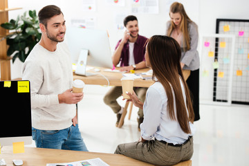selective focus of multicultural colleagues with coffee to go and business people behind in office