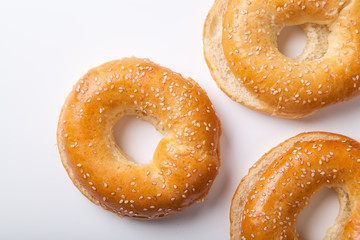 Three fresh baked bagle buns with sesame seeds on white background pre-cut for making sandwiches