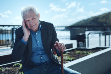 Chronic headache. Tired old man sitting outdoors and massaging his temple while suffering from a...