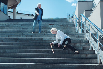 Are you ok. Mindful senior husband shouting to his wife while seeing her falling down on stairs and feeling pain in her leg.