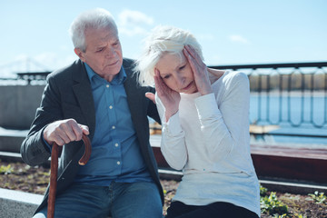 Love is the key to healing. Mindful husband hugging his wife and trying to soothe her severe pain while both sitting outdoors near the riverwalk.