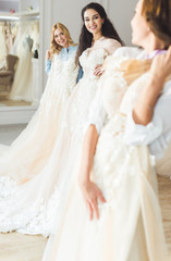 Obraz na płótnie Canvas Young brides holding dresses in wedding atelier