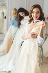 Naklejka premium Smiling women with wedding dresses in wedding salon