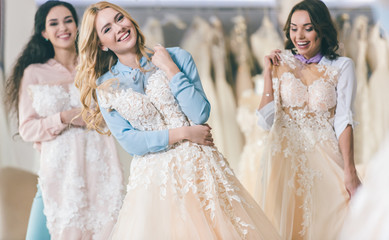 Young smiling bride and bridesmaids choosing dresses in wedding salon