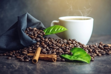 White black espresso Cup with pile of coffee beans and green leaves in bag on dark background