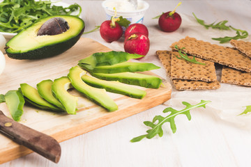 Green ripe avocado on wooden chopping board. Red garden radish, arugula, eggs and rye bread crusts. Healthy food