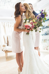 Smiling women in wedding dresses embracing in wedding atelier