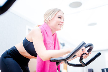 Beautiful sport young woman working out on the exercise bike at the gym, intense cardio workout.