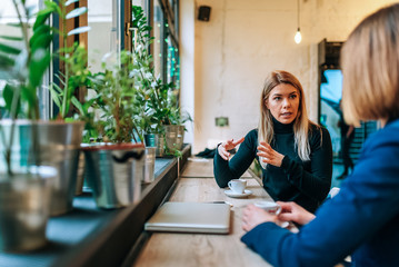 Two friends enjoying a cup of coffee as they sit at the table near the window.