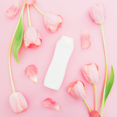 Shampoo and white tulips flowers on pink background. Flat lay, top view