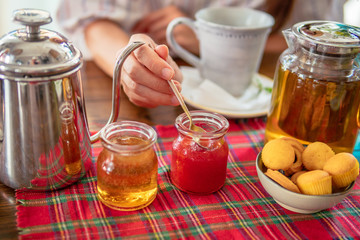Tea drinking. Woman eat homemade strawberry jam.Tea pot, honey, muffins on table