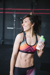 Fototapeta na wymiar Fit brunette tired woman resting and drinking after training working out in Gym