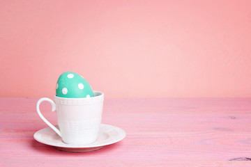 Coffee cup with Easter egg on a pink table.