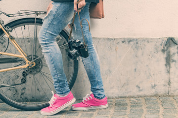Girl with a bicycle and retro camera posing on the street.
