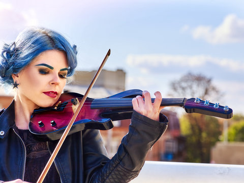 Woman perform music on violin in park outdoor. Girl performing jazz on city street. Spring outside with blue hairstyle background. Good hobbies for people.