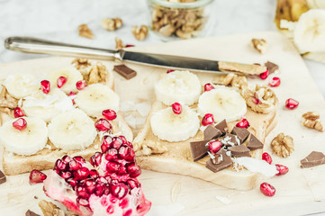 Sandwich with peanut butter, banana slices and chocolate on wooden cutting board