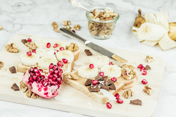 Sandwich with peanut butter, banana slices and chocolate on wooden cutting board