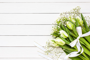 Bouquet of white tulips and gipsophila decorated with ribbon on white wooden background. Top view, copy space