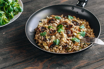 Risotto with bacon, mushrooms and greens in a frying pan on a wooden table