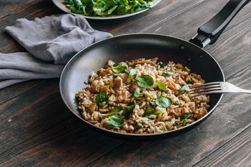 Risotto with bacon, mushrooms and greens in a frying pan on a wooden table