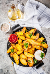 baked fried potatoes with garlic, herbs, red and white sauces, on grey stone background copy space top view