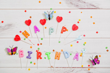 Candle, butterfly and confetti on wooden background. Birthday holiday concept.