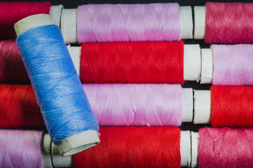 Spool of blue thread on the background of spools of pink and red thread