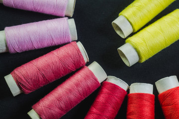 Spools of red, pink and yellow sewing thread on black material 