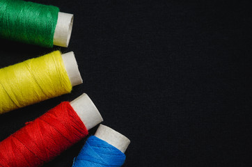 Spools of red, blue, green and yellow sewing thread on black material