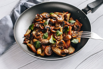 Fried potatoes with mushrooms and greens in a frying pan on a wooden table vegetarian food