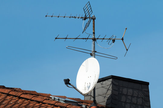 Satellitensch&uuml;ssel und alte Antenne auf einem roten Dach