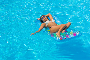 portrait of pretty young woman in swimsuit lying on a inflatable mattress at pool.