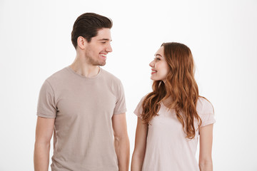 Portrait of happy people 20s man and woman having relationship wearing beige t-shirts looking at each other with loving gaze and smile, over white background