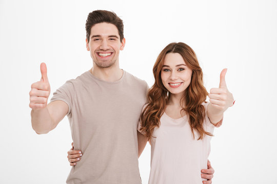 Portrait Of Pleased Caucasian People 20s Man And Woman Wearing Beige T-shirts Posing Together On Camera With Happy Smile And Showing Thumbs Up, Over White Background