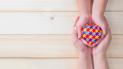 World Autism Awareness day, mental health care concept with puzzle or jigsaw pattern on heart with autistic child's hands supported by nursing family caregiver