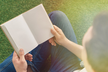 cropped shot of young man reading book while sitting on grass