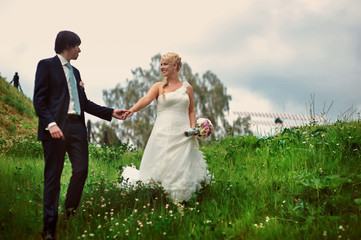 Bride and groom at wedding Day walking Outdoors on summer nature. Bridal couple, Happy Newlywed woman and man embracing in green park. Loving wedding couple outdoor. Bride and groom in honeymoon