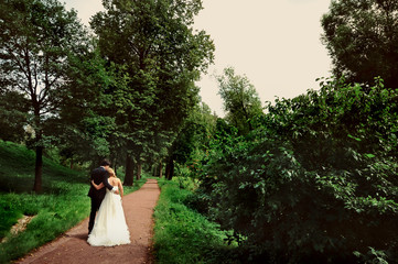 Bride and groom at wedding Day walking Outdoors on summer nature. Bridal couple, Happy Newlywed woman and man embracing in green park. Loving wedding couple outdoor. Bride and groom in honeymoon