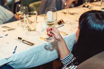 woman holds glass of white wine. people consider the color of the wine and try how it smells in different glasses
