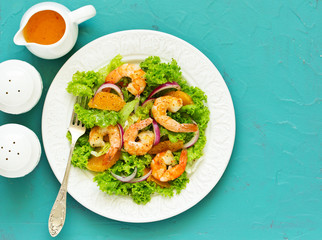A plate of lettuce, with slices of orange, red onions, and prawns with vinaigrette dressing. A dietary dish.