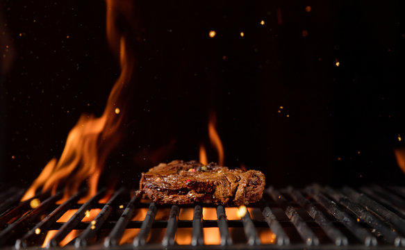 Fiery grill grid with piece of beef steak.