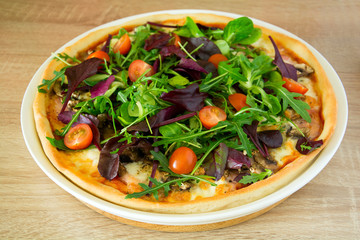 Pizza with arugula, salad mix and cherry tomatoes on wooden table