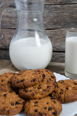 Oatmeal chocolate chip cookies, jug and glass of milk, rustic wooden background.