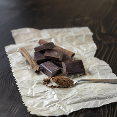 Broken chocolate bar and spices on wooden table.