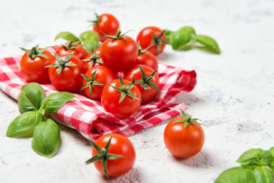 Fresh cherry tomatoes with basil leaves on a stone table with red checkered towel, healthy food